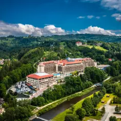 Widok z lotu ptaka na duży hotel Gołębiewski otoczony zielonymi wzgórzami i rzeką.